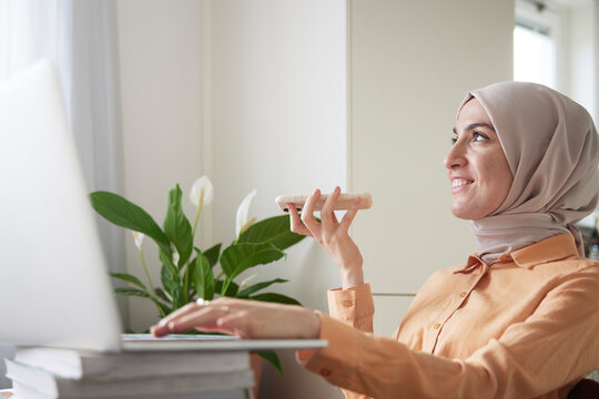 Smiling woman with hijab having conversation on speaker mode on her cell phone