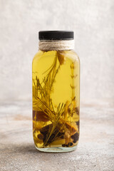 Sunflower oil in a glass jar with various herbs and spices on a brown concrete. Side view.