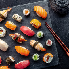 Sushi overhead square shot with chopsticks and tea. Rolls, maki, nigiri on a black background, Japanese food. Salmon, tuna, eel, shrimp and other seafood