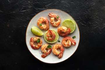 Shrimps, overhead flat lay shot. Fried shrimp with lime on a plate, shot from the top on a black slate background. Gourmet dish