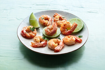Shrimps. Cooked shrimp with lime on a white plate, on a teal blue table. Spicy gourmet meal