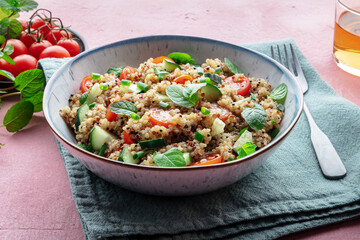 Quinoa tabbouleh salad in a bowl, a healthy dinner with tomatoes and mint, on a pink background