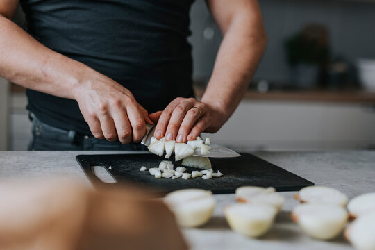 Man's hands chopping onions on cutting board in kitchen