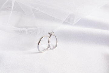 Obraz na płótnie Canvas Front view of two platinum and diamond engagement rings against the background of the bride's wedding veil and soft folds of satin white fabric.