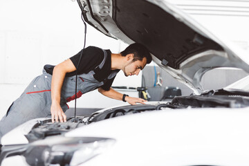 Car mechanic working in workshop checking engine