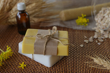 Fototapeta na wymiar Handmade soap bars, wax candle, oil essential, oats and fresh flowers. Natural ingredients for homemade facial and body mask or scrub. Healthy skin care. SPA concept. Selective focus. Side view.