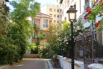 Ruelle pittoresque dans la Cité Florale, dans la ville de Paris, ensemble de rues végétalisées avec de nombreuses fleurs, arbres et plantes vertes dans de petits jardins devant les maisons (France)