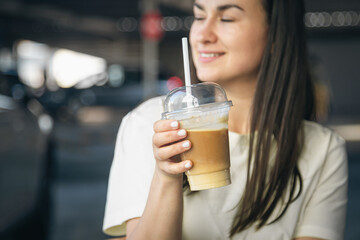 Close-up, disposable cup of iced coffee in female hands.
