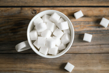 Cup with sugar cubes on a wooden surface, close-up.