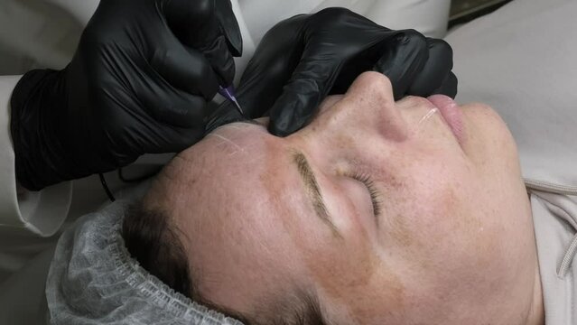 Close-up of microblading process: art of eyebrow tattooing. With gloved hands, skilled practitioner wields aspecialized needle, embedding pigment into skin. eyebrows are meticulously tinted using