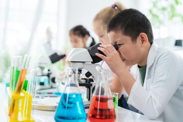 Young Asia scientist boy wearing lab coat and using microscope to see the structure of leaf In the...