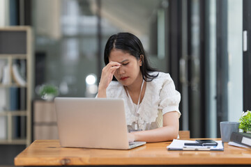 Stressed Financier a asian woman at works, uses a laptop, makes a report to a finance company. Accounting and financial concept