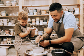 Pottering with son. Confident young man and little boy making ceramic pot on the pottery class