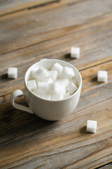 Cup with sugar cubes on a wooden surface, close-up.