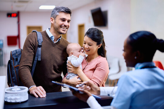 Happy family with baby communicating with reception nurse at medical clinic.