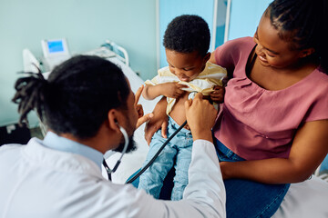 Black pediatrician examining kid with stethoscope during medical appointment at doctor's office.