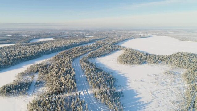 Winter in Finland; slow backward drone flight over a snow covered landscape with forests and frozen lakes in southern Lapland. 