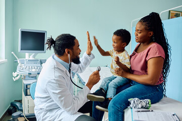 Happy black boy gives high five to his pediatrician after medical examination at doctor's office.