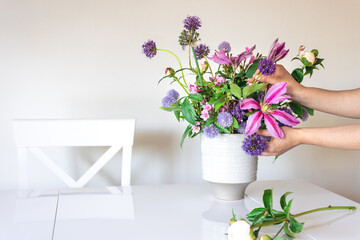 Vase with fresh summer flowers in female hands on a white background.
