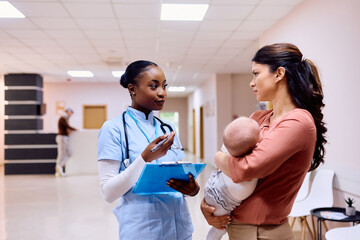 Black pediatric nurse talks to mother with baby at doctor's office.