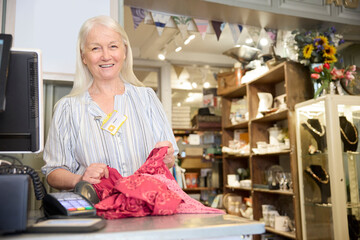 Portrait Of Senior Female Volunteer Working In Charity Shop Or Thrift Store Selling Used And Sustainable Clothing