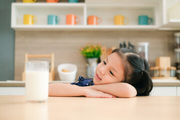 Little cute girl with glass of milk on  table in the kitchen.