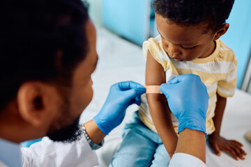 Close up of black kid getting band aid after vaccination at pediatrician's.