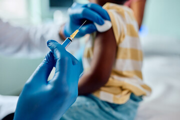 Close up of black pediatrician giving vaccine to kid at doctor's office.