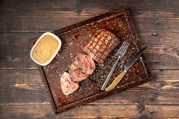 Sliced grilled beef tenderloin seasoned with salt, rosemary and thyme on a wooden cutting board