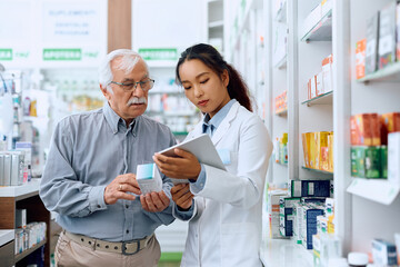 Senior man and his pharmacist using touchpad while looking for medicine in drugstore.