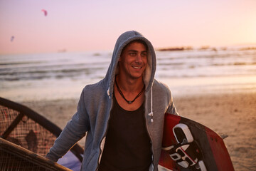 Smiling man in hoody carrying kiteboard on beach