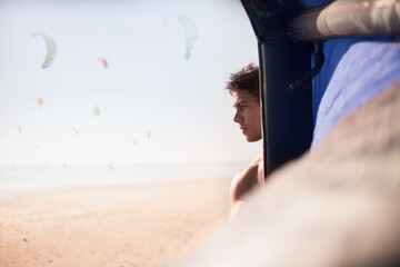 Pensive man looking away behind kiteboarding kite on sunny beach