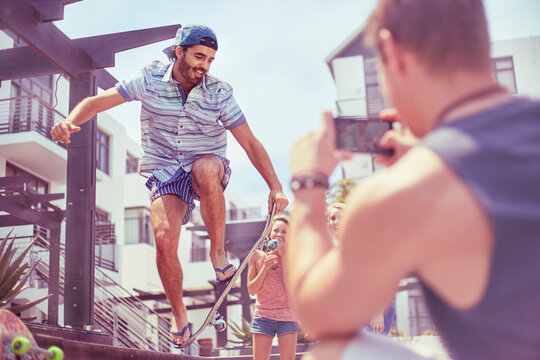Young man photographing friend doing skateboard stunt