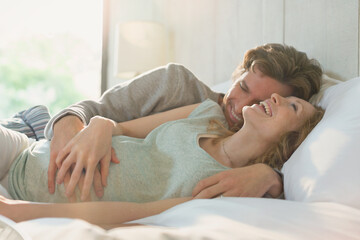 Affectionate pregnant couple laying in bed laughing