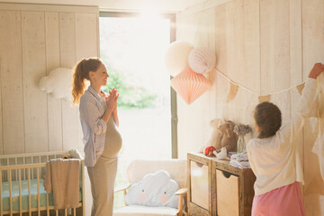 Pregnant mother and daughter decorating sunny nursery - obrazy, fototapety, plakaty