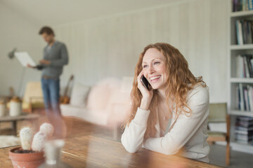 Fototapeta premium Smiling woman talking on cell phone at dining table