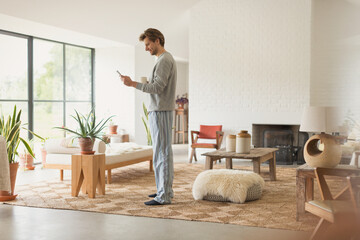 Man in pajamas drinking coffee and using digital tablet in living room