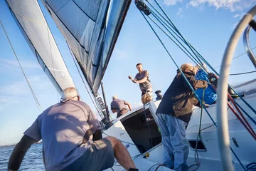 Zelfklevend Fotobehang Men sailing adjusting rigging and sail on sailboat © KOTO