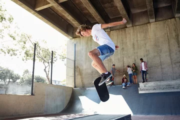 Ingelijste posters Teenage boy flipping skateboard at skate park © KOTO