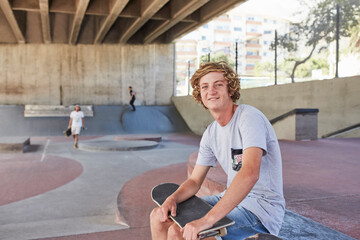 Portrait smiling teenage boy with skateboard at skate park