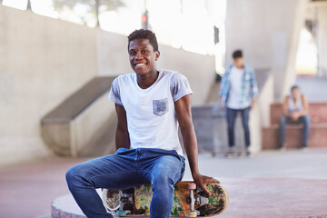 Portrait smiling teenage boy sitting on skateboard at skate park