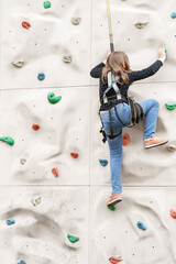 Teenage teen girl grabbing artificial high climbing wall with split ledges. Climbing harness safety...