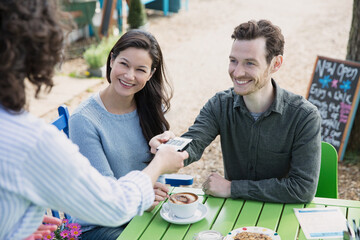 Waitress handing credit card reader to couple at outdoor cafe