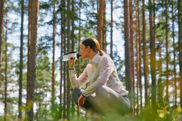 Runner resting drinking water bottle in woods