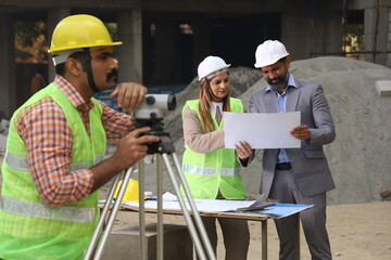 Fototapeta na wymiar Indian construction workers. Construction engineers working on a builder construction site. Wearing white and yellow helmet analyzing blueprint of property. Reporting, maintaining the work in progress