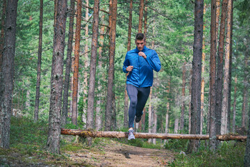 Obraz premium Runner jumping over fallen tree on trail in woods
