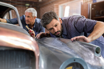 Focused mechanic examining classic car panel in auto repair shop