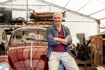 Portrait confident mechanic leaning on classic car in auto repair shop