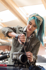 Young female mechanic blue hair fixing car engine in auto repair shop - obrazy, fototapety, plakaty