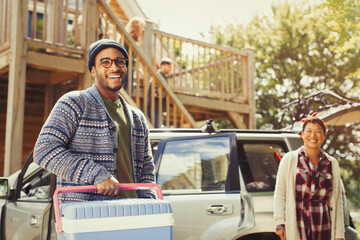 Portrait smiling couple unloading cooler from car outside cabin